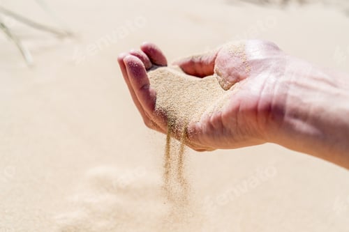 Preview: A hand pouring sand on a desert sand dune. Sand slips sifting through fingers