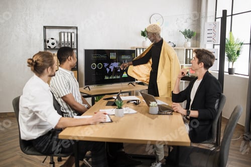 Preview: Group of four partners sitting at desk and listening speech of african american man near monitor