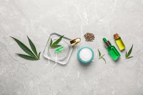 Preview: Hemp cosmetics and green leaves on light table, flat lay