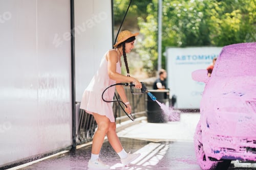 Preview: Brunette from a high-pressure hose applies a cleaner on the car