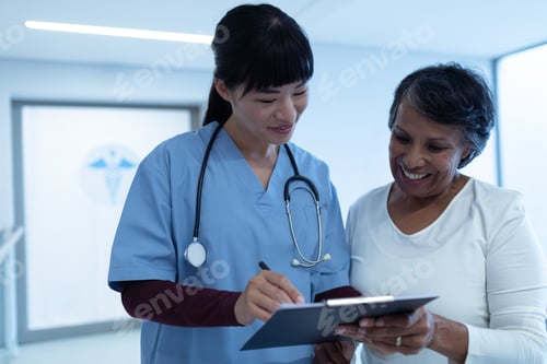 Preview: Asian female doctor interacting with mixed-race female patient in the corridor