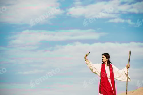 Preview: handsome man in jesus robe talking selfie while holding wooden cane
