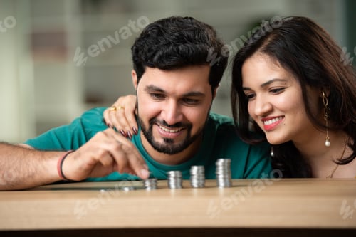 Preview: Indian asian young couple saving coins on table, front view