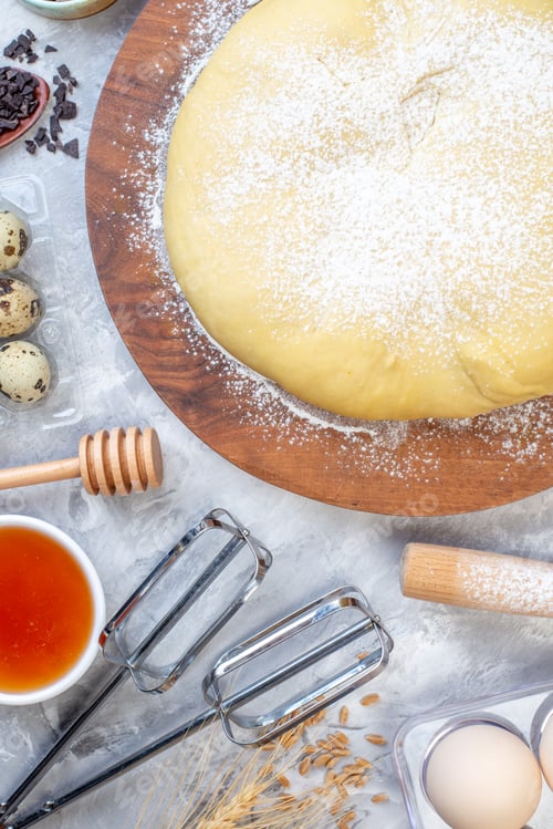 Preview: Overhead view of raw pastry flour on round board honey eggs on stained white background