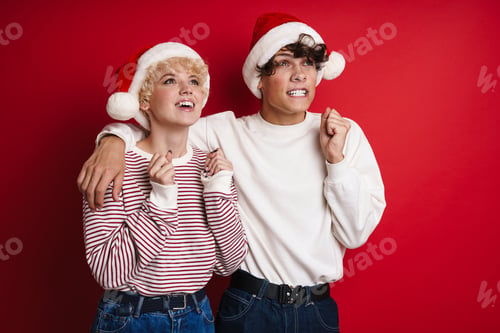 Preview: Excited couple in Santa Claus hats hugging and holding clinched fists
