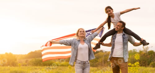 Preview: Beautiful family with the American flag in a field at sunset. Independence Day, 4th of July.