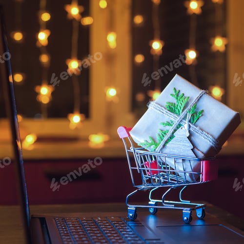 Preview: Online shopping concept. Miniature shopping cart with gift box on laptop