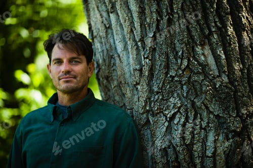 Preview: A man standing by a large tree with gnarled ridged bark.