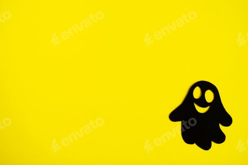 Preview: Holiday decorations for Halloween. Black paper ghost on a yellow background, top view.