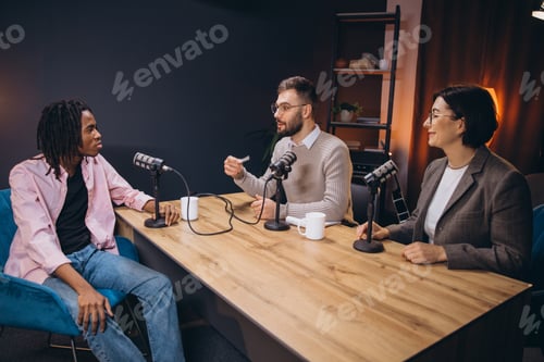 Preview: Podcasters recording audio content at wooden table inside professional studio setting