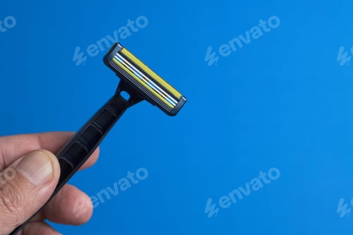 Preview: Hand Holding a Razor Against a Bright Blue Background for Grooming Needs