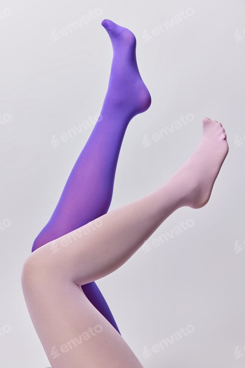 Preview: Slender female legs in different color pantyhose raised up in air against white background