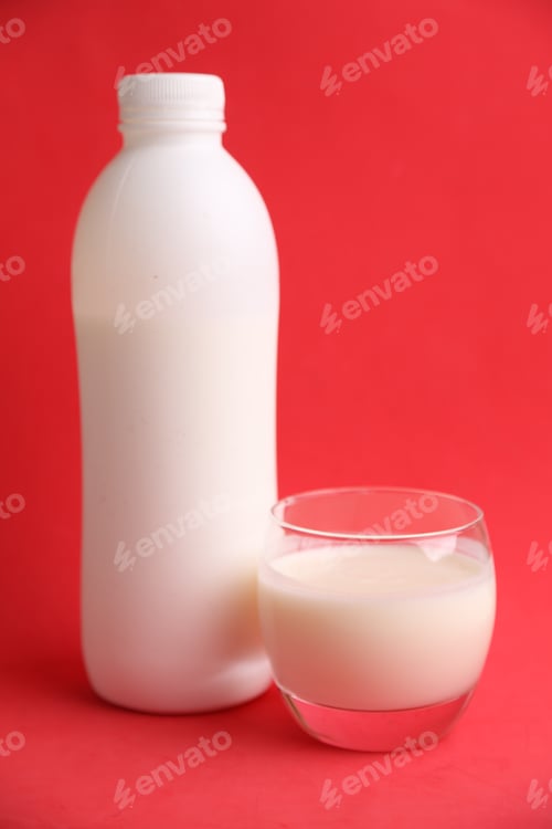 Preview: Vertical shot of a white plastic bottle and a glass of milk isolated on a red background