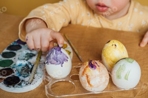 Preview: A small child paints Easter eggs with fingers in multi-colored paints