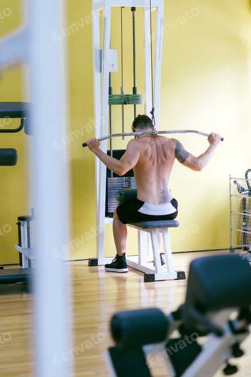 Preview: Fit man on lat pull down machine at the health club. Work out on Pull down Weight Machine