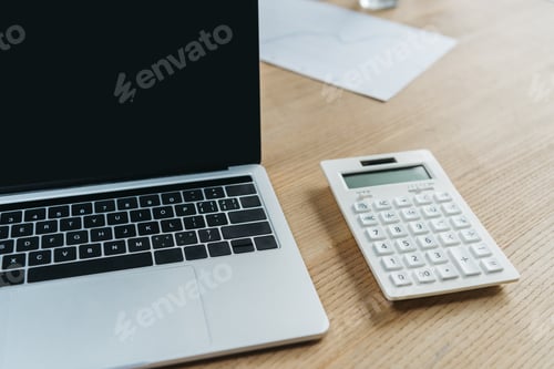 Preview: laptop with blank screen and calculator on wooden table