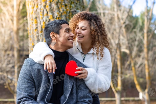 Preview: two people embracing and holding a red heart near a tree