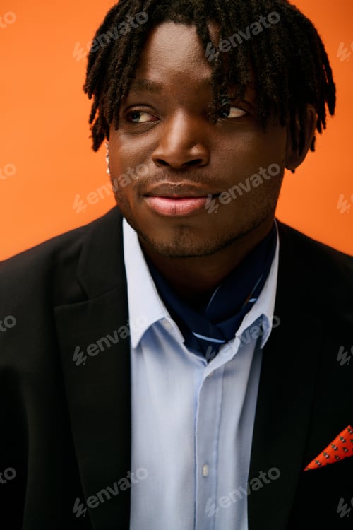 Preview: Young man in fashionable attire poses with confidence against a vibrant orange backdrop