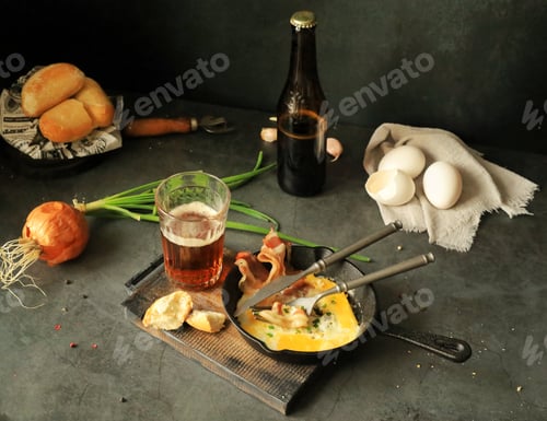 Preview: Fried eggs with bacon in a frying pan on the table, beer and other food products for lunch