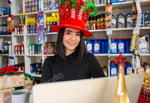 Preview: Young woman smiling in auto parts store while wearing festive christmas hat