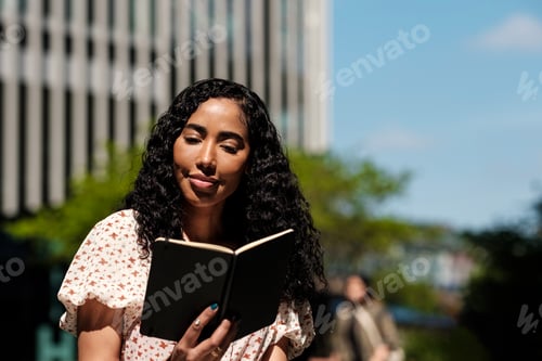 Preview: Relaxed curly woman is reading a book outdoors.