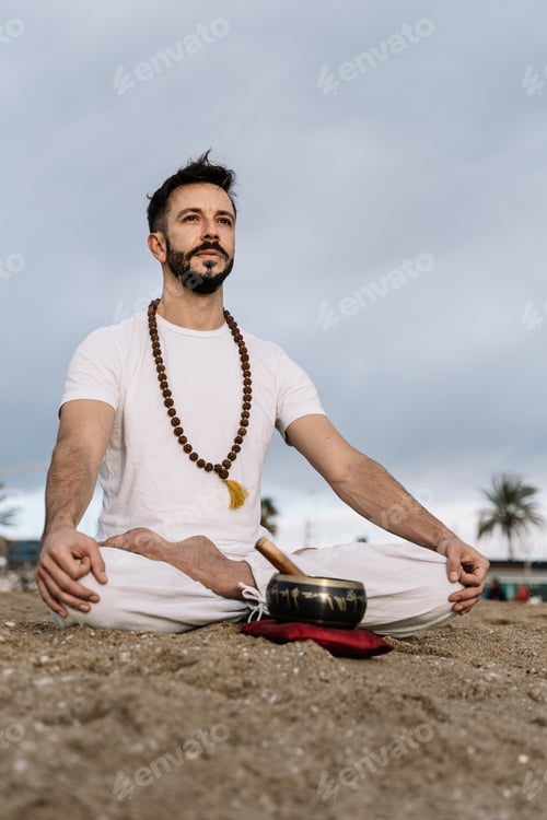 Preview: Caucasian man with beard practicing meditation exercises on the beach at dawn