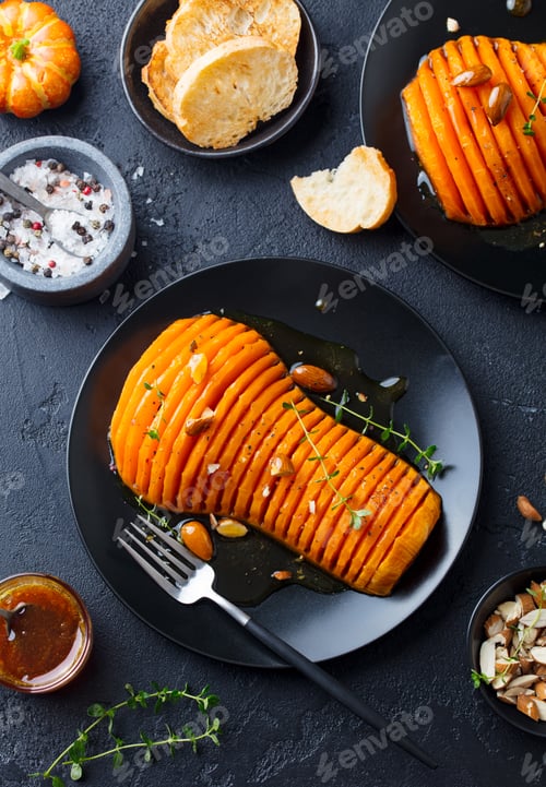 Preview: Roasted Pumpkin with Honey Glaze and Herbs on a Black Plate. Dark Background. Top view.