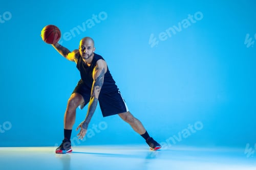 Preview: Young basketball player training isolated on blue studio background in neon light