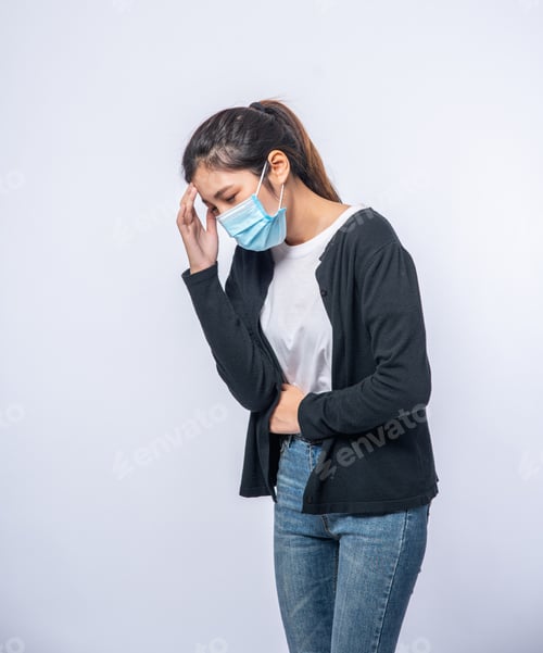 Preview: A sick woman with a headache wore a mask and placed a hand on her head.