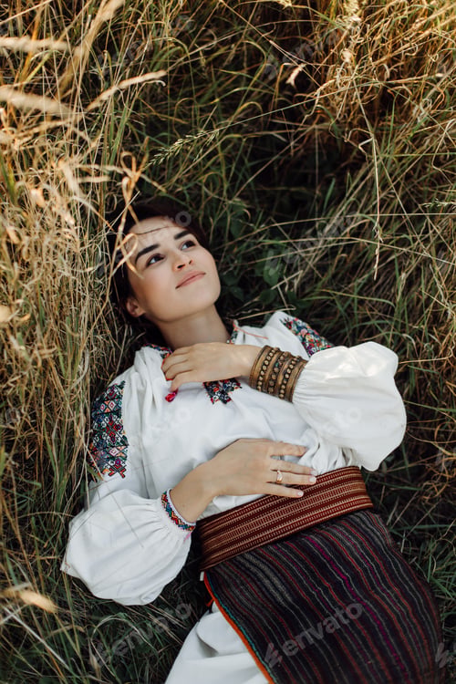 Preview: Young woman in traditional national embroidered shirt and skirt on nature at sunset.