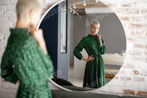 Preview: Woman in green dress looks at herselfes in the mirror at home