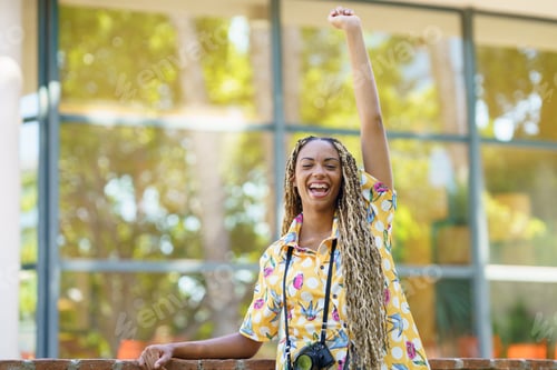 Preview: African girl with braids, raising her arm in joy. Girl holding a camera.