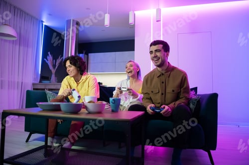 Preview: Young friends play video games while sitting on a couch in a living room