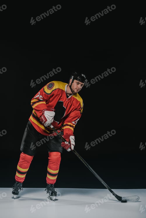 Preview: full length view of handsome young sportsman in protective sportswear playing hockey on black