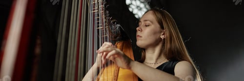 Preview: Header Image of Female Musician Playing Harp with Passion in Dim Light in Church