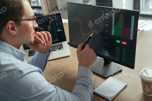 Preview: Concentrated man trader pointing pen at pc monitor with diagram of stock crypto currency market