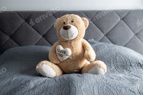 Preview: Teddy bear perched on a gray bed
