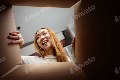 Preview: Happy Young Woman Excitedly Looks Into Cardboard Box