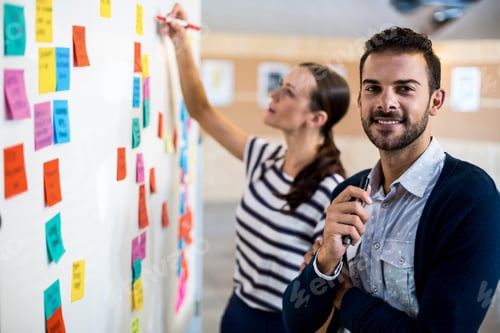 Preview: Young man smiling at camera while colleague writing on white board