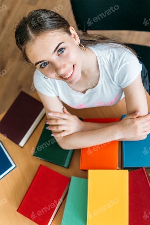 Preview: Back to school library concept. Student girl holding book on her head on the background of