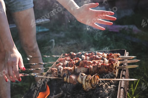 Preview: Juicy meat on barbecue skewers cooking by young woman in backyard in summer. Food background. BBQ N