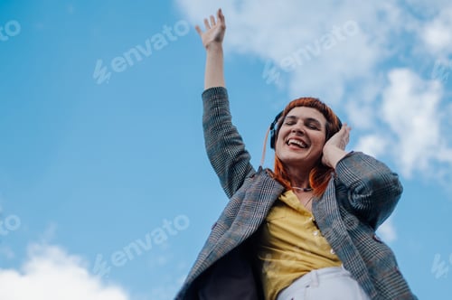Preview: Happy businesswoman listening to music with headphones and dancing under blue sky