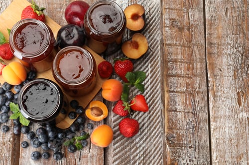 Preview: Different jams in jars and ingredients on wooden table, flat lay. Space for text
