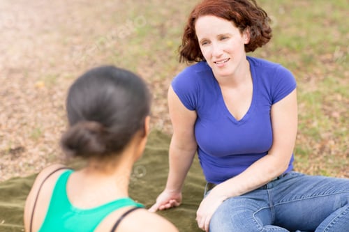Preview: High angle view of young woman sitting on picnic blanket talking to friend, smiling