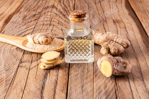 Preview: Homemade natural ginger root oil in bottle with a cork cap on a wooden background among ginger roots