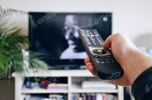 Preview: A person holding a remote control to switch channel on tv