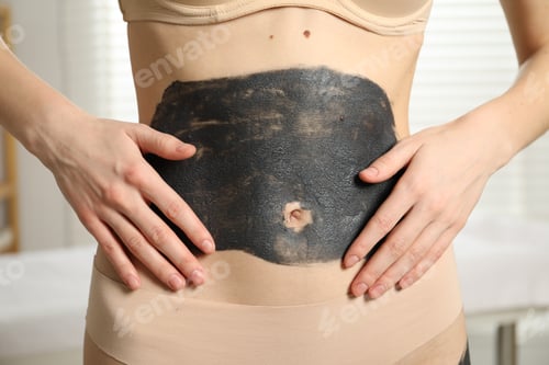 Preview: Woman doing spa body wraps on her belly in salon, closeup