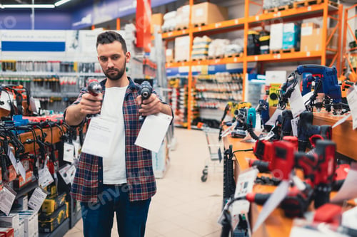 Preview: a male customer in a hardware store in the power tool department compares two screwdrivers