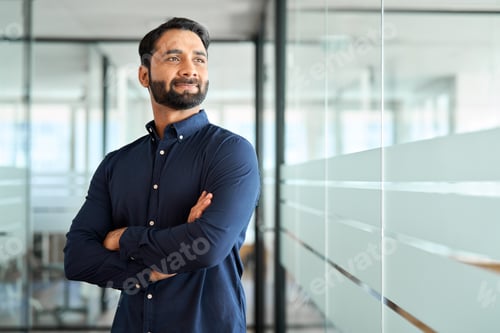 Preview: Confident Indian business man leader looking away standing in office hallway.