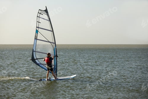 Preview: Windsurfer against the backdrop of the setting sun, on calm water, goes calmly along the sea, active